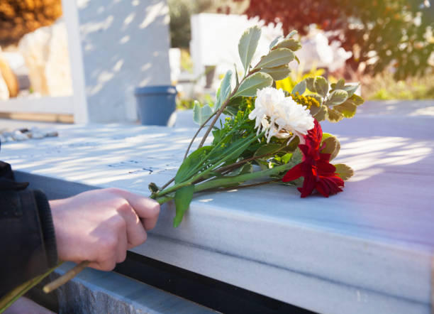istock Man's hand with flowers near tombstone. 831493962
