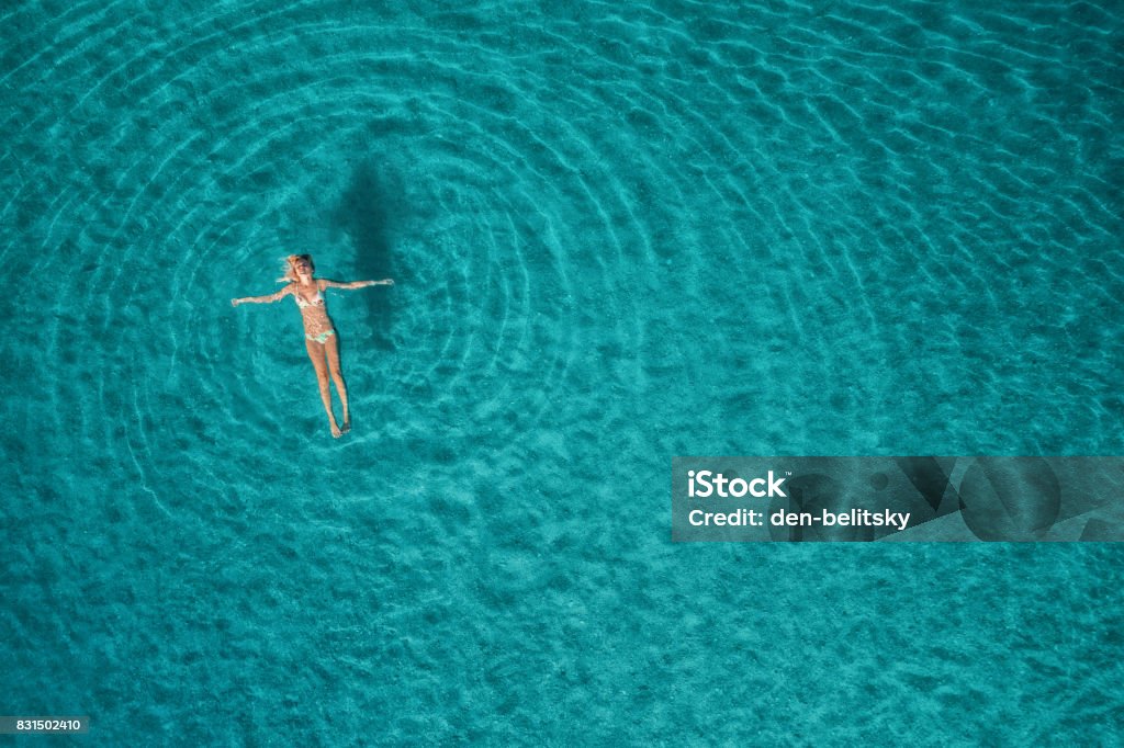 Aerial view of swimming woman in Blue Lagoon. Mediterranean sea in Oludeniz, Turkey. Summer seascape with girl, clear azure water, waves at sunrise. Transparent water.Top view from flying drone.Travel Swimming Stock Photo