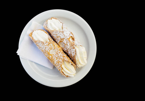 Two canoli with butter cream laid out on a plate over black background stock photo