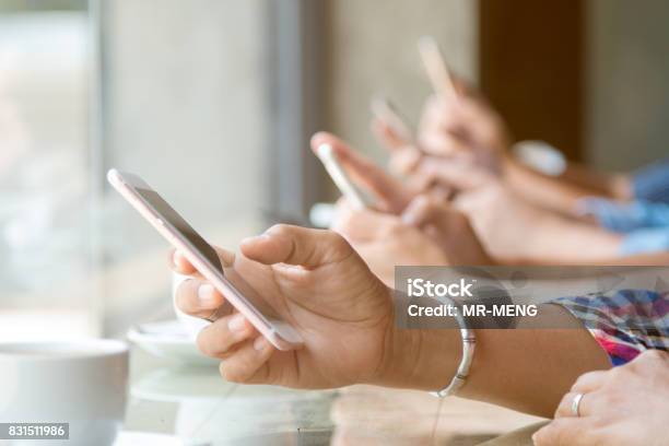 Close Up Of Four People Hand Holding Mobile Phone And Using Internet In Coffee Shop With Warm Light Flare Stock Photo - Download Image Now