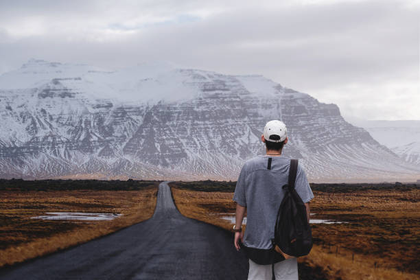 istock Young man with backpack walking alone on the country road 831514244