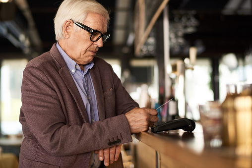 Side view portrait of modern senior man paying via contactless bank card in cafe