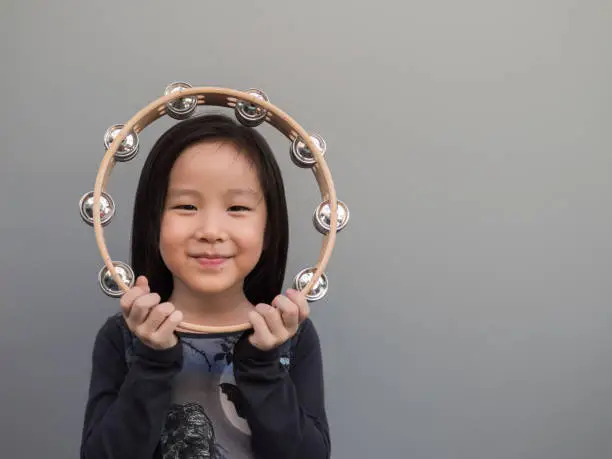 Little asian child play the tambourine, gray background