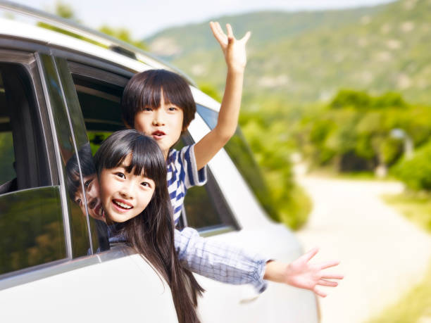 two asian children waving hands while traveling by car