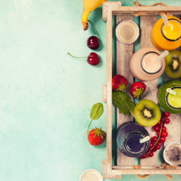 Fresh juices or smoothies with fruits and vegetables in wooden tray on blue background