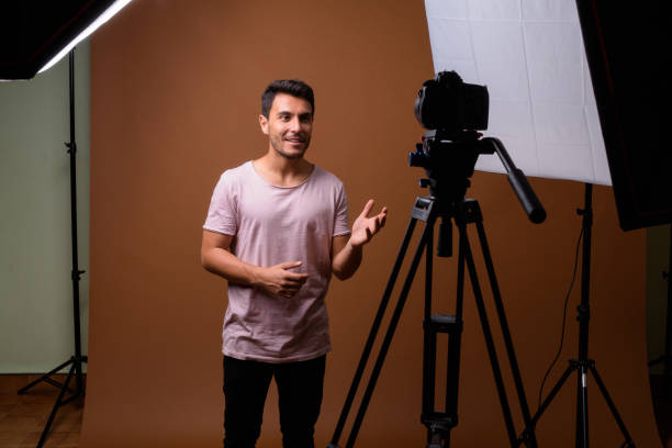 istock Studio shot of young handsome Hispanic man vlogging while wearing pink shirt against colored background 831584856