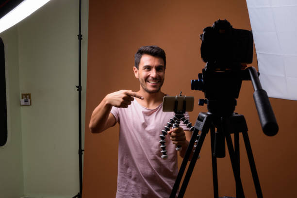 istock Studio shot of young handsome Hispanic man vlogging while wearing pink shirt against colored background 831584934
