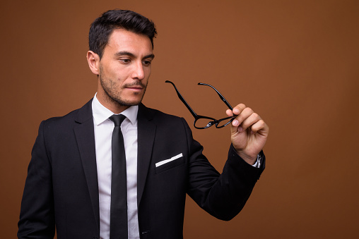 Studio shot of young handsome Hispanic businessman against colored background horizontal shot