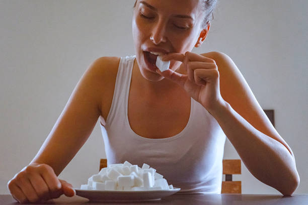 Close-up of a young woman eating sugar cubes from the plate before her stock photo