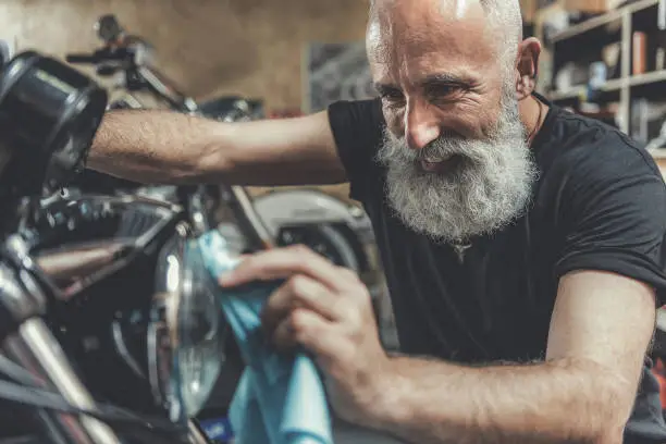 Photo of Happy smiling old man cleaning motorbike