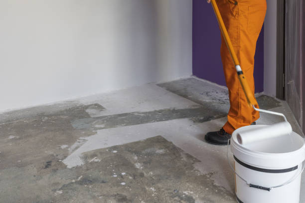 istock Interior of apartment under construction. Man holding a roller and puts primer on concrete floor 831590250