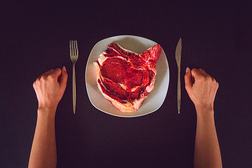 High angle view image of a female hands on the table, beside the plate with served raw rib eye steak.