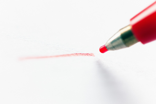 Macro shot of a red fineliner drawing a line on white paper with copy space.