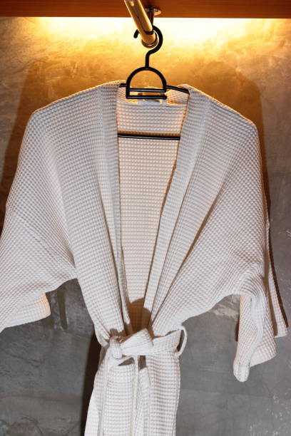 istock Bathrobe hanging on clothes hanger against warm white light background. 831597058