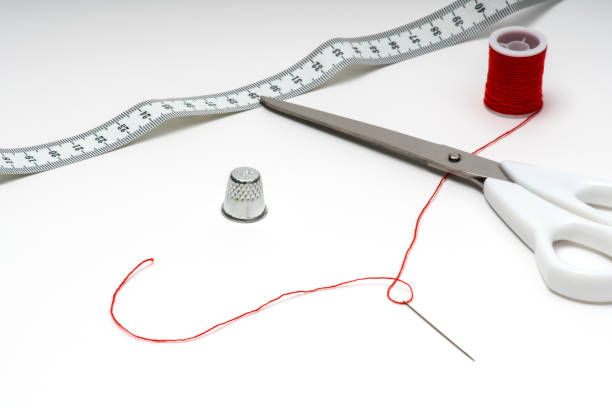 Tailor tools on white table with red thread Scissors, thimble, measuring tape and skein with thread in needle's eye needles eye stock pictures, royalty-free photos & images