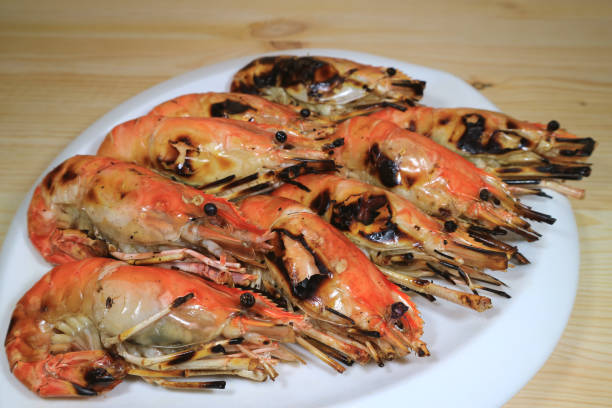 istock Flaming Grilled Whole River Prawns on White Plate Served on Wooden Table, with Selective Focus 831605432