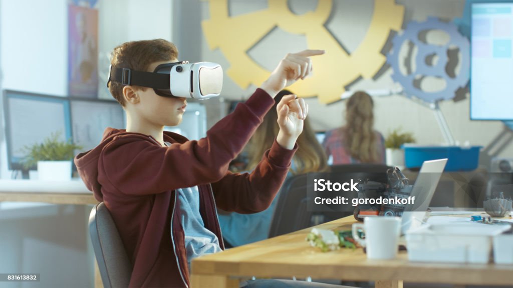 In a Computer Science Class Boy Wearing Virtual Reality Headset Works on a Programing Project. Virtual Reality Simulator Stock Photo