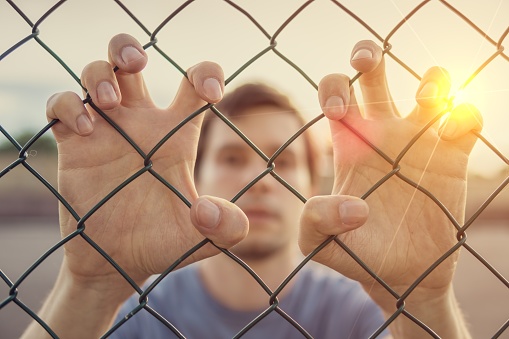 Young man behind wired fence. Immigration concept.