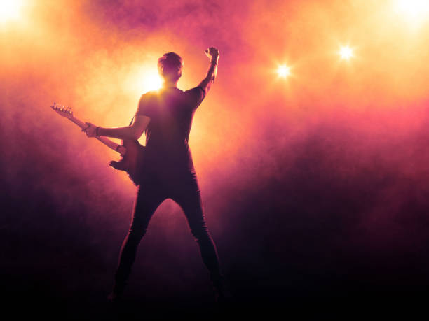 Guitarist playing a guitar on stage Silhouette of guitar player on stage on orange background with smoke and spotlights bass instrument stock pictures, royalty-free photos & images