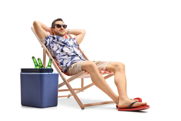 Tourist relaxing in a deck chair next to a cooling box filled with bottles of beer isolated on white background