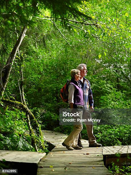 Mature Couple Standing On Pathway In Forest Stock Photo - Download Image Now - 55-59 Years, Adults Only, Boardwalk