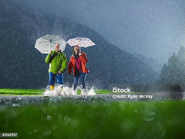 Mann Und Frau Mit Sonnenschirmen Spielen Im Regen Stockfoto und mehr Bilder von Regen - Regen, Pfütze, Regenschirm