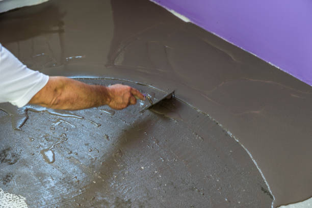 istock Worker puts a self leveling screed with tool on concrete floor. House under construction 831631824