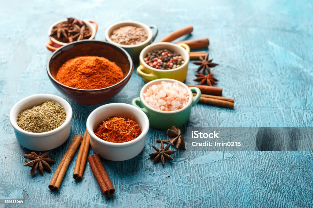Spices and condiments in small bowls Dry colorful spices and condiments anise, paprika, saffron, pepper, salt, bay leaf, cinnamon in small bowls on blue background Spice Stock Photo