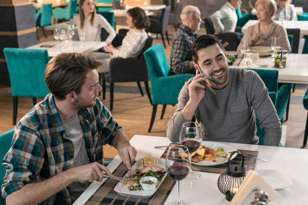 istock Young businessman talking on cell phone while eating dinner with friend 831639956