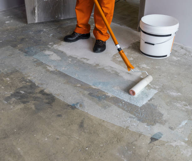 istock Worker puts primer with roller on concrete floor in room from unfinished apartment 831643580