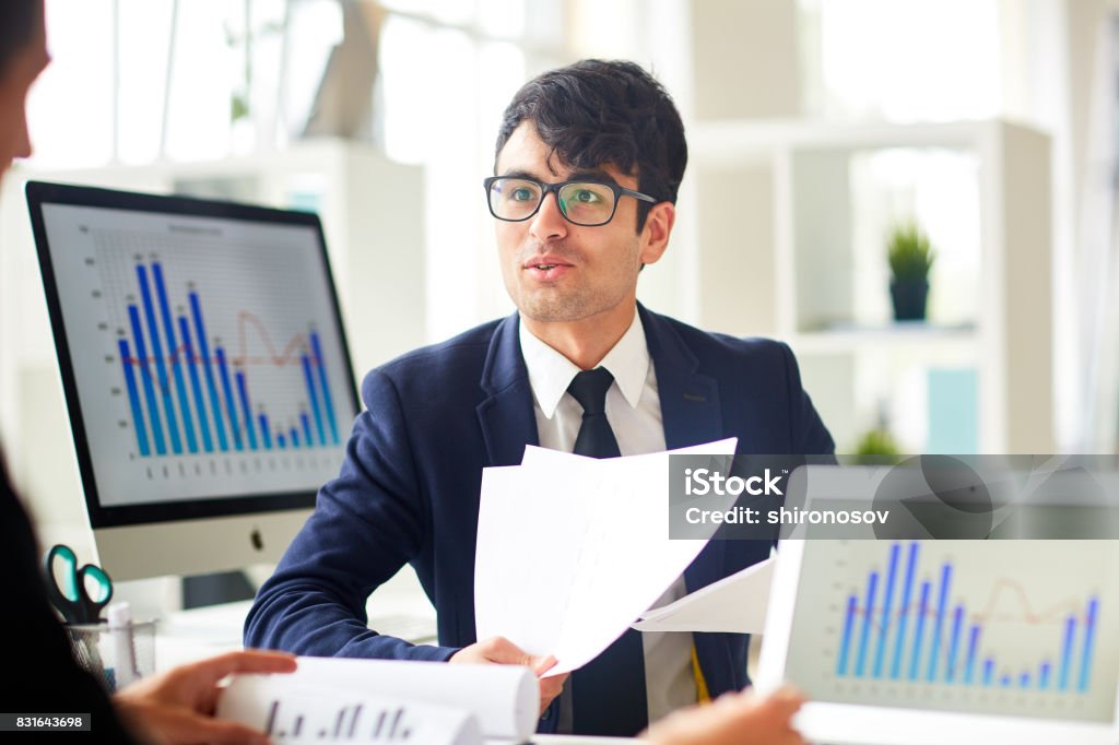 Consulting with colleague Young economist talking to colleague and explaining financial papers Economist Stock Photo