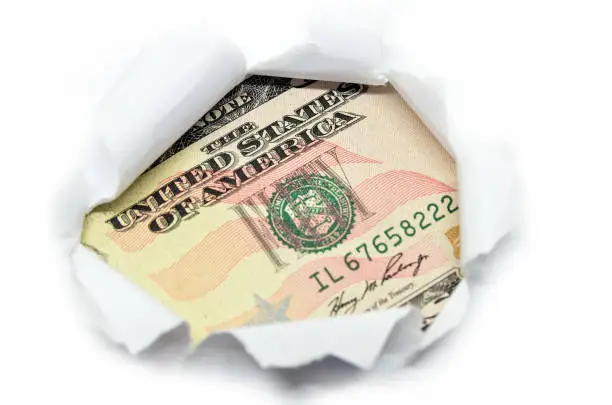 Photo of US currency macro peeking through torn white paper.