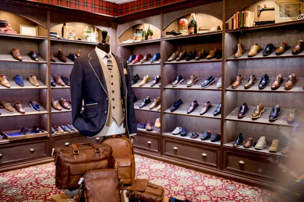 Interior of a high-quality shop for men with shoes on display. A cosy luxurious atmosphere. A mannequin on display wearing a blazer, waistcoat, shirt and tie. leather man bags also on show.