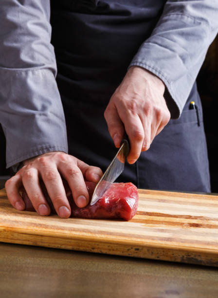 istock Chef cutting filet mignon on wooden board at restaurant kitchen 831668596