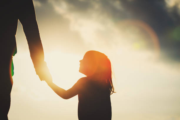 silhouette of little girl holding parent hand at sunset stock photo