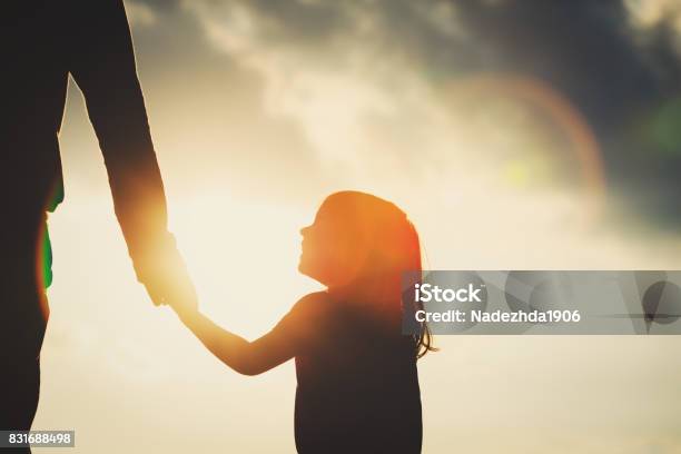 Silhouette Of Little Girl Holding Parent Hand At Sunset Stock Photo - Download Image Now