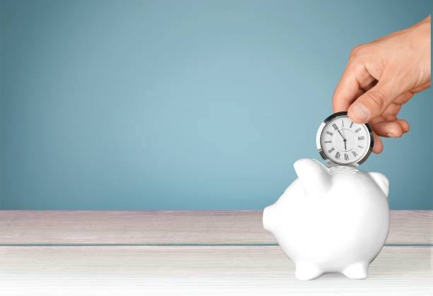 Time. Hand depositing clock in piggy bank on background savings account stock pictures, royalty-free photos & images