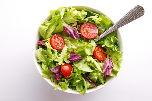 Fresh salad in a bowl. Healthy lettuce and tomato meal on a white background. Top view
