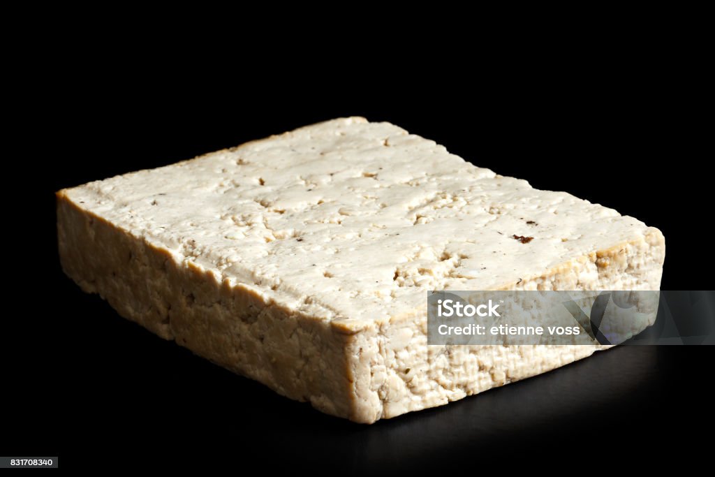 Single block of lightly smoked tofu isolated on black. Asian Food Stock Photo