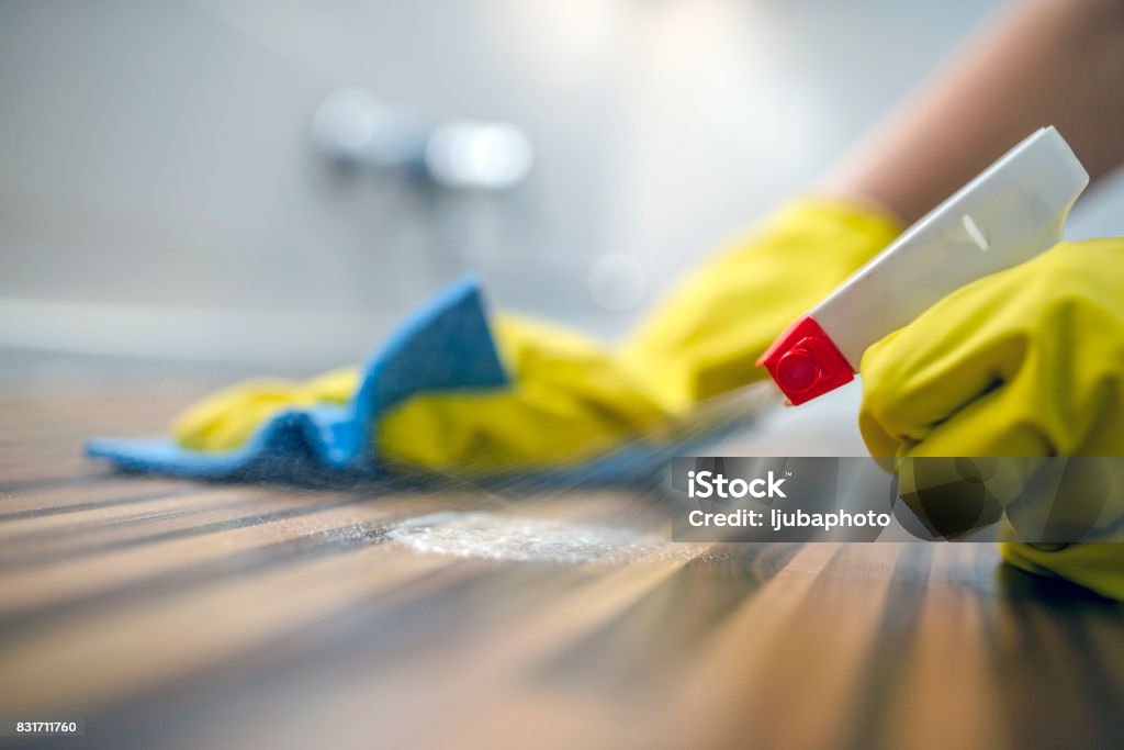 Cleaning kitchen table  with blue cloth Photo of Woman or man cleaning kitchen cabinets with sponge and spray cleaner. Female or male hands Using Spray Cleaner On Wooden Surface. Maid wiping dust while cleaning her house wearing yellow protective gloves, close-up Cleaning Stock Photo