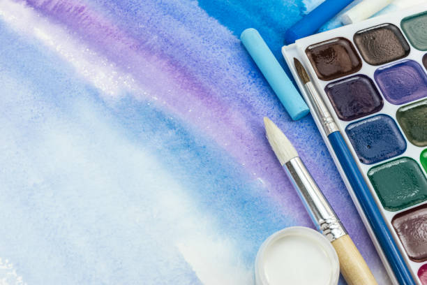 istock paints palette with paintbrushes and pastel crayons on blue watercolor background 831716216