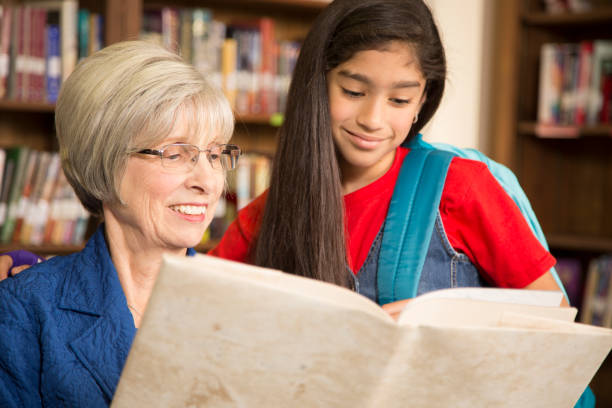 istock Teacher, librarian reads book to elementary student in library or classroom. 831727804