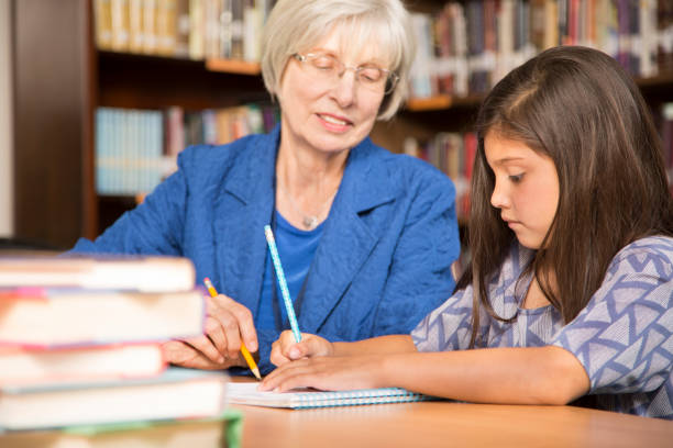 istock Teacher, mentor helps elementary-age schoolgirl with homework. 831727842