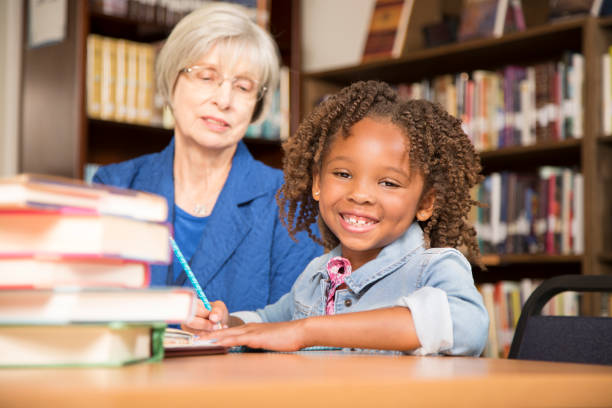 istock Teacher, mentor helps elementary-age schoolgirl with homework. 831727914