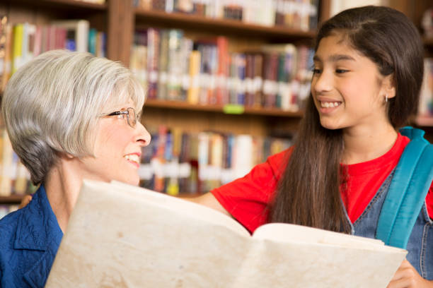 istock Teacher, librarian reads book to elementary student in library or classroom. 831728082
