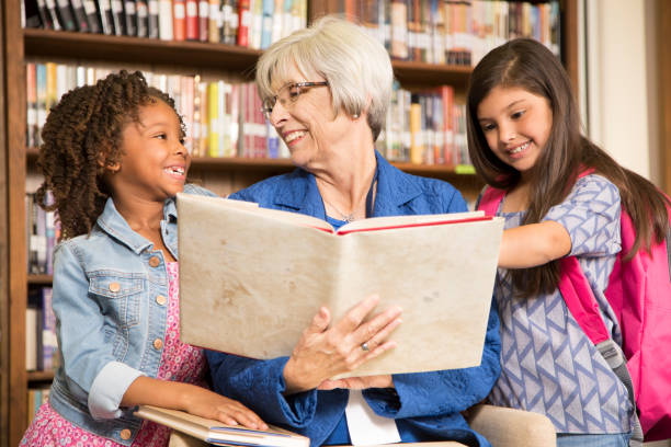 istock Teacher, librarian reads book to elementary students in library or classroom. 831728252