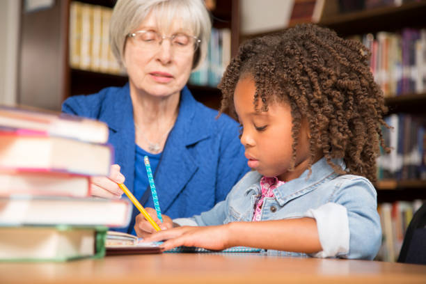 istock Teacher, mentor helps elementary-age schoolgirl with homework. 831728618