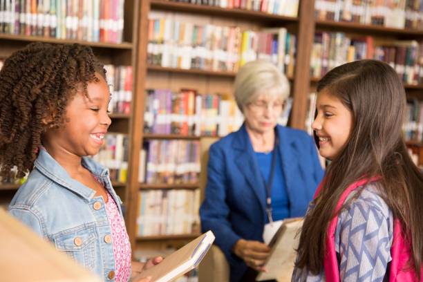 istock Elementary age girls choose books in school library. 831729006