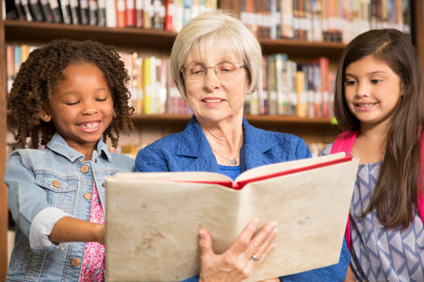 istock Teacher, librarian reads book to elementary students in library or classroom. 831729084