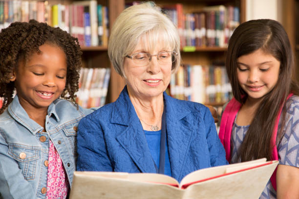 istock Teacher, librarian reads book to elementary students in library or classroom. 831729318